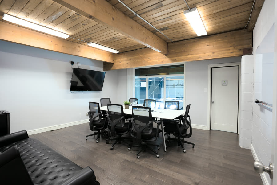 Studio A's conference room, a wood-topped table with black mesh chairs beneath an exposed timber ceiling
