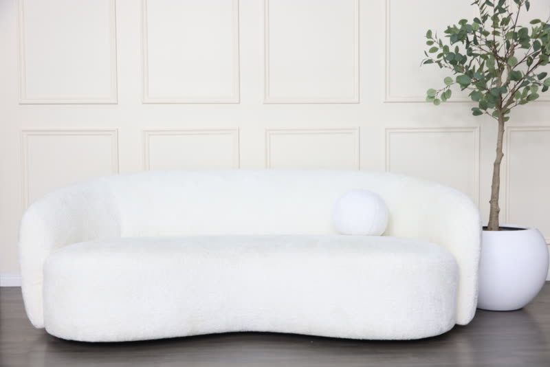 Studio A's living room set: a curved white boucle sofa with a potted tree against a panelled wall